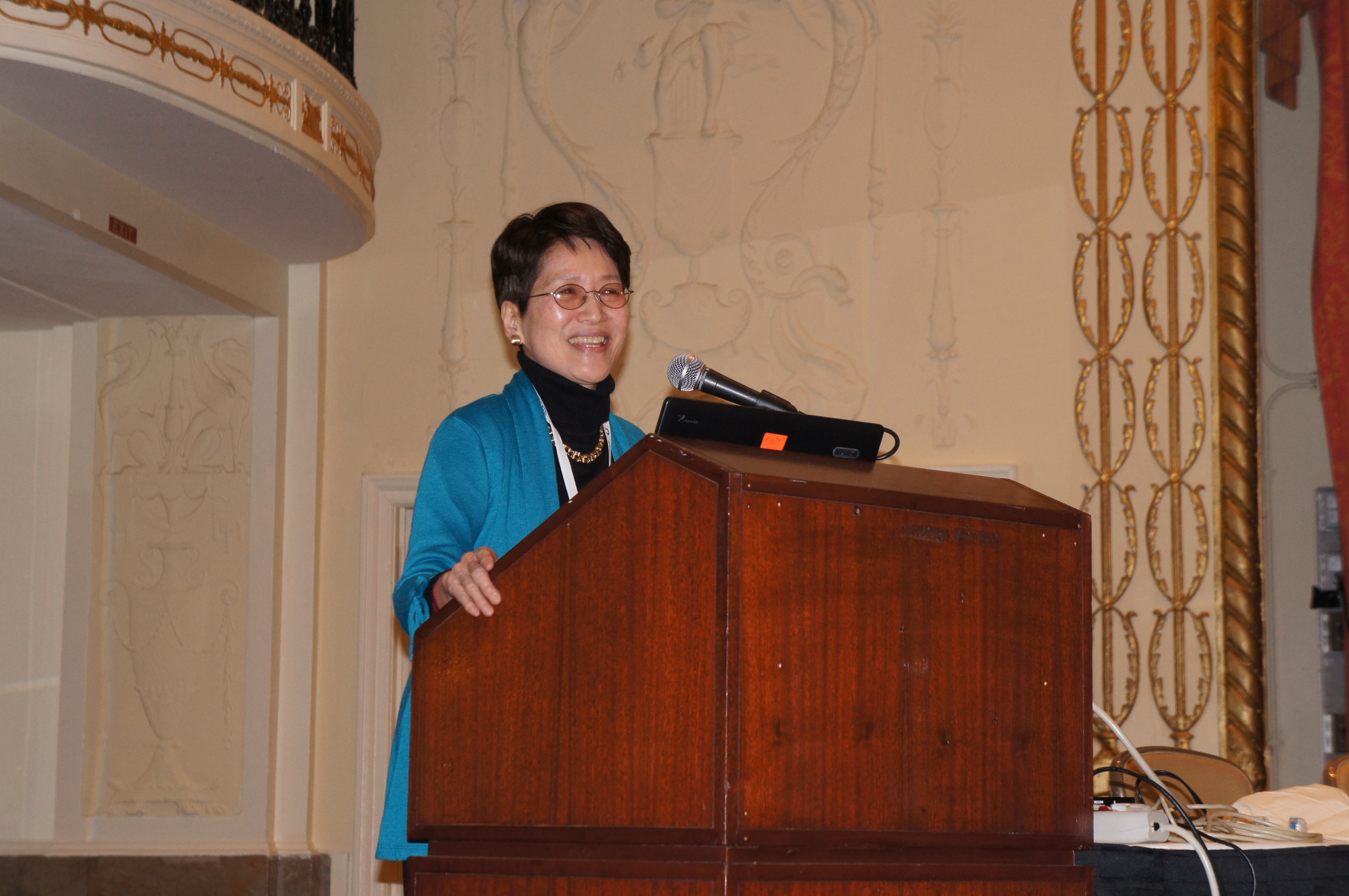 Image of female with glasses in blue blazer speaking at a podium