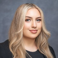 Image of female with blonde hair in a black blazer in front of a gray background.