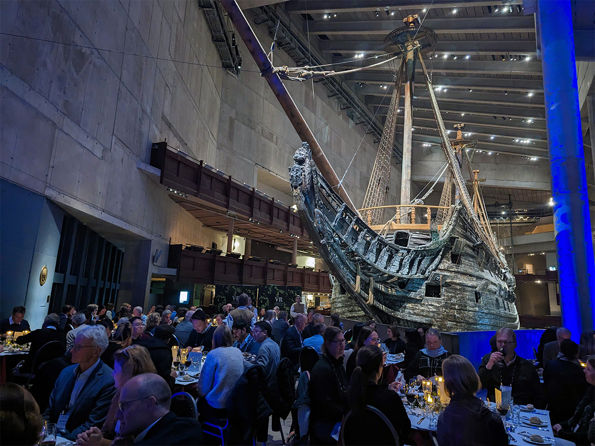 Biopharmaceutical attendees eating dinner around tables in the Vasa Museum with a ship hanging in the background for a dinner reception for CMC Strategy Forum Europe 2023.