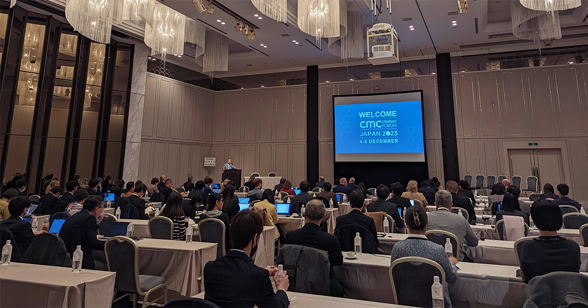 Biopharmaceutical attendees sitting at tables in a large ballroom listening to a welcome presentation at CMC Strategy Forum Japan 2023.