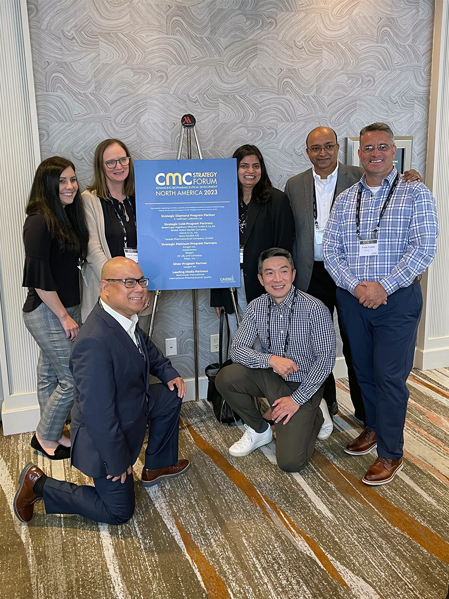 Biopharmaceutical scientists smiling and posing next to a CMC Strategy Forum North America 2023 sign.