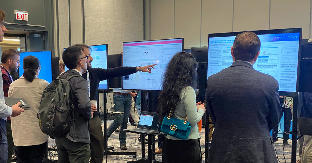 Biopharmaceutical scientists pointing at and discussing scientific poster presentations on digital monitors at HOS 2023 and Mass Spec 2023.