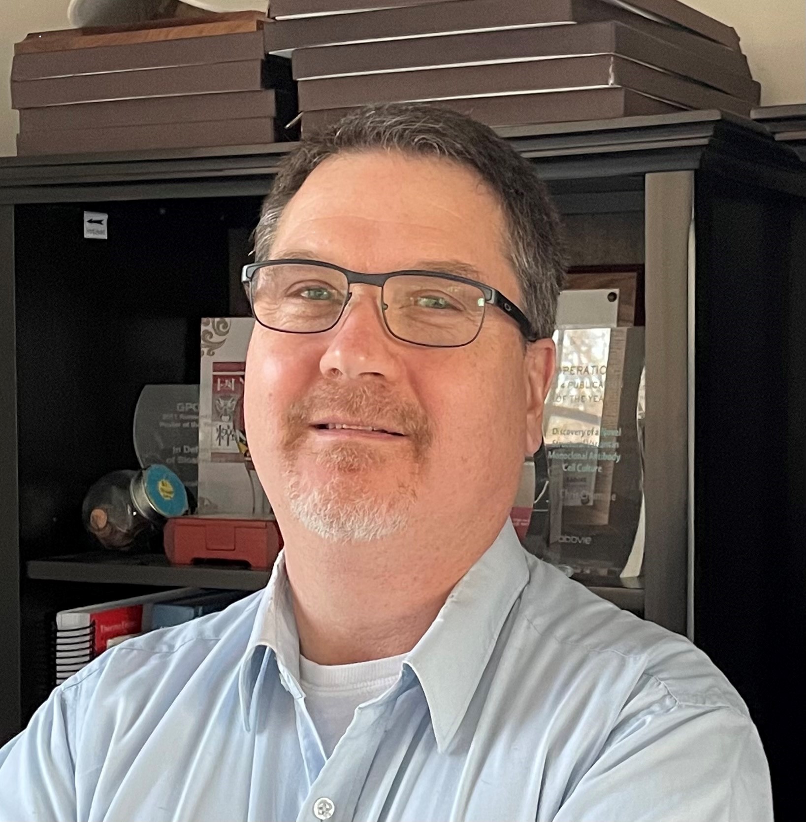 Image of one male in professional attire standing in front of a bookcase.