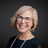 Image of woman with blonde hair wearing glasses in front of black background.