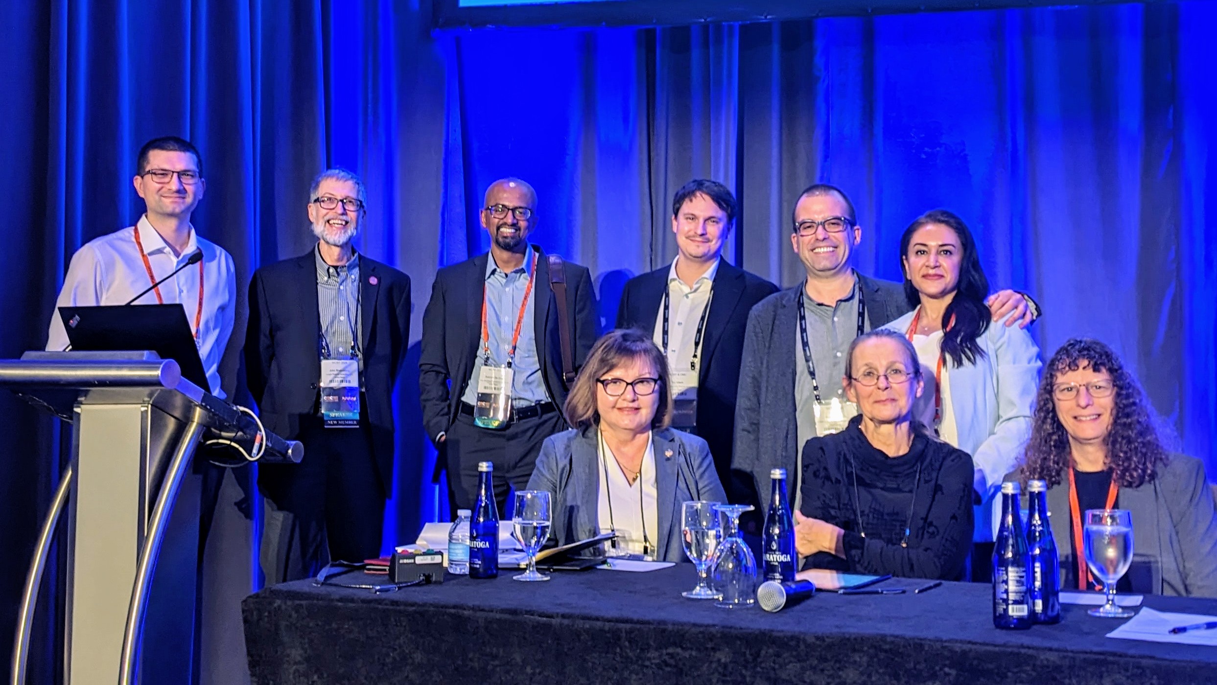 BIopharmaceutical scientists standing and sitting at table on a stage to present at WCBP Symposium 2024.